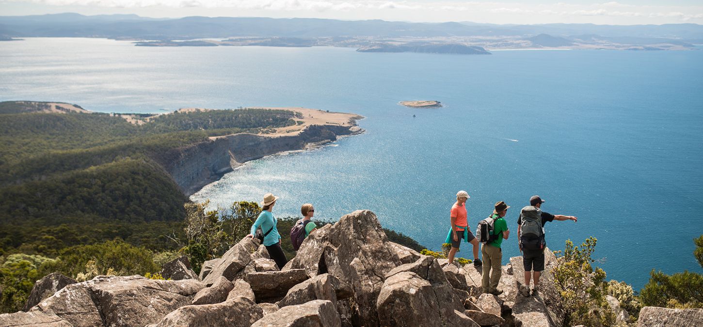 Guests atop rocks overlooking Wineglass Bay and ocean